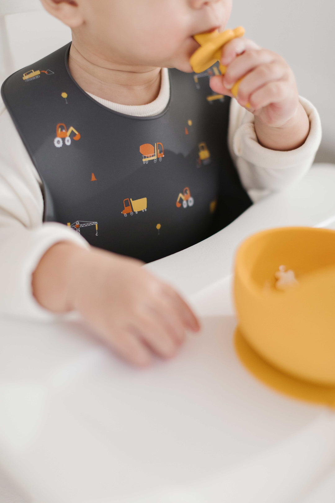 Baby Eating Cereal with charcoal gray silicone bib with construction trucks on it